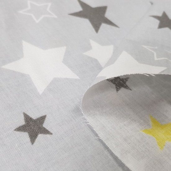 Tela Algodón Estrellas Decorativas Gris - Tela de algodón con dibujos decorativos de estrellas de color blanco, gris oscuro y amarillo sobre un fondo de color gris. La tela mide 160cm de ancho y su composición 100% algodón.