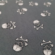 Cotton Pirate Skulls fabric - Cotton fabric with drawings of white pirate skulls on a black background and also in grey background. The fabric is 145cm wide and its composition 100% cotton.