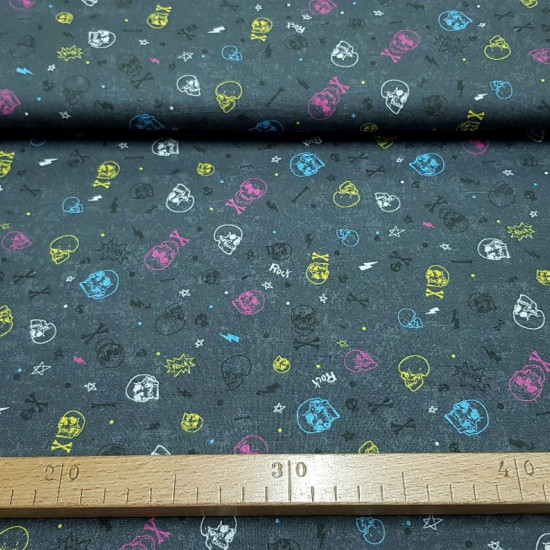 Cotton Rock Skulls fabric - Cotton fabric with drawings of various colored skulls on a dark gray background with Rock letters, multi-colored rays and bones. The fabric is 150cm wide and its composition is 100% cotton.