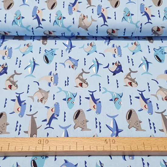 Cotton Funny Sharks fabric - Children's cotton fabric with drawings of sharks and other fishes on a light blue background decorated with small waves. The fabric is 140cm wide and its composition is 100% cotton.