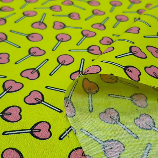 Tela Algodón Piruletas Corazones - Tela de algodón con dibujos de piruletas con forma de corazón sobre un fondo verde lima. La tela mide 150cm de ancho y su composición 100% algodón.