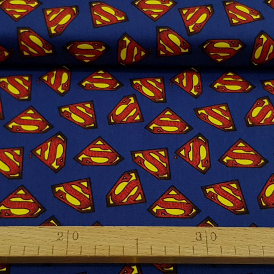 Tela Algodón Superman Logos Azul - Tela de algodón ancho americano con dibujos de logotipos del superhéroe Superman sobre fondo azul. La tela mide 110cm de ancho y su composición 100% algodón