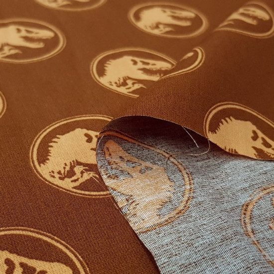 Tela Algodón Jurassic Logos Cognac - Tela de algodón con dibujos de logos de Jurassic Park sobre un fondo de color naranja cognac. La tela mide 150cm de ancho y su composición 100% algodón.