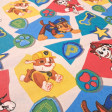 Tela Algodón Patrulla Canina Escudos Algodón Patrulla Canina Escudos - Tela de popelín algodón licencia con dibujos de los personajes de Patrulla Canina sobre un fondo de formas de colores y escudos. La tela mide 140cm de ancho y su composición 100% algodón.