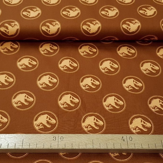 Tela Algodón Jurassic Logos Cognac - Tela de algodón con dibujos de logos de Jurassic Park sobre un fondo de color naranja cognac. La tela mide 150cm de ancho y su composición 100% algodón.