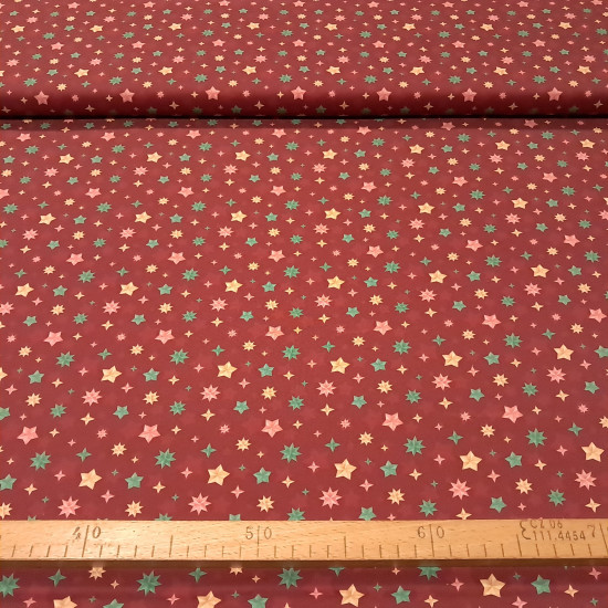 Cotton Christmas Stars Wishes fabric - Cotton poplin fabric with Christmas star designs in different shapes and colors on a red/maroon background. The fabric is 150 cm wide and is made of 100% cotton.