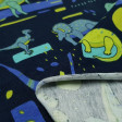 Tela Punto Algodón Dinosaurios Abstracto - Tela de punto algodón tipo camiseta con dibujos de dinosaurios en colores verdes y azules sobre un fondo azul oscuro con formas abstractas. La tela mide 150cm de ancho y su composición 95% algodón – 5% Elastano