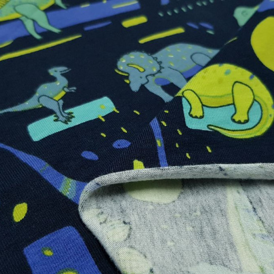 Tela Punto Algodón Dinosaurios Abstracto - Tela de punto algodón tipo camiseta con dibujos de dinosaurios en colores verdes y azules sobre un fondo azul oscuro con formas abstractas. La tela mide 150cm de ancho y su composición 95% algodón – 5% Elastano