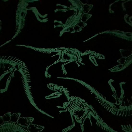 Tela Softshell Dinosaurios Brilla en la Oscuridad - Tela Softshell con dibujos de esqueletos de dinosaurio, que se ilumina en la oscuridad. El color del fondo es un azul oscuro. La tela Softshell es una tela funcional que se compone de 3 capas, la capa ex
