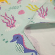 Tela Punto Algodón Orgánico Sirenas - Tela de punto algodón orgánico (GOTS) con dibujos de sirenitas, caballitos de mar, medusas… sobre un fondo de color claro. La tela mide 160cm de ancho y su composición 95% algodón – 5% elastano