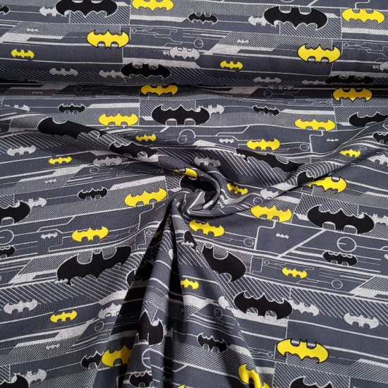 Tela Punto Algodón Batman Logos - Tela de punto algodón licencia con dibujos de logos de Batman en varios colores y tamaños sobre un fondo donde predominan los colores grises. La tela mide 150cm de ancho y su composición 92% aglodón – 8% elastano.