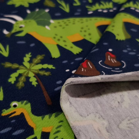 Tela Punto Algodón Dinosaurios Volcanes - Tela de punto algodón tipo camiseta con dibujos de dinosaurios, vegetación y volcanes sobre un fondo azul oscuro. La tela mide 150cm de ancho y su composición 95% algodón - 5% elastano.