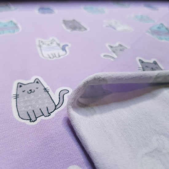 Punto Camiseta Gatitos Lila - Tela de punto algodón tipo camiseta con dibujos de gatos sonrientes sobre un fondo lila. La tela mide 145cm de ancho y su composición 95% algodón - 5% elastano.