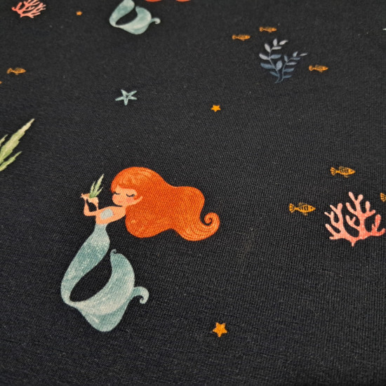 Cotton Jersey Sirens fabric Cotton Jersey Sirens fabric - Cotton jersey fabric with a digital print featuring mermaids, seaweed, and starfish on a dark blue background. The fabric is 140 cm wide and is made of 95% cotton and 5% elastane.
