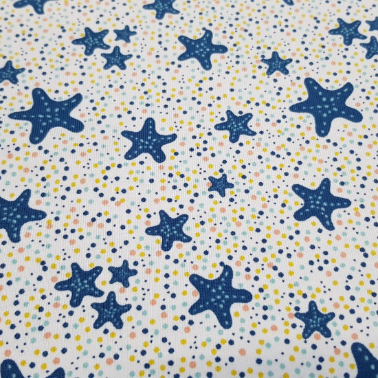 Tela Punto Camiseta Estrellas de Mar - Tela de punto algodón orgánico tipo camiseta con dibujos de estrellas de mar en color azul sobre un fondo blanco con topitos de colores. La tela mide 150cm de ancho y su composición 95% algodón - 5% elastano.
