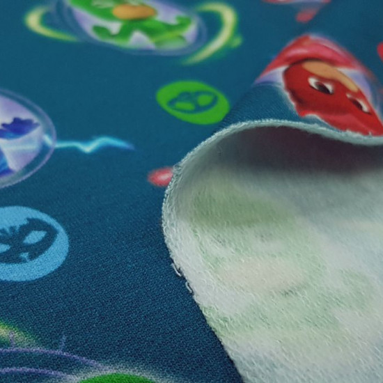 Tela Punto Sudadera PJ Mask - Tela de punto tipo sudadera con dibujos de los personajes PJ Masks sobre un fondo azul petroleo. La tela mide 160cm de ancho y su composición 95% algodón - 5% elastano