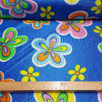 Tela Rasete Flores Hippies - Colorida tela de disfraz brillante y fina con dibujos de flores de colores sobre fondo azul. La tela es un tejido rasete/trilobal que no se deshila y es fácil de cortar. Tejido ideal para confeccionar disfraces llamativo