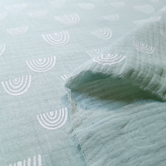 Double Gauze White Strokes fabric - Double gauze or muslin fabric with white outlined rainbow patterns on a mint green and oker background. The fabric is 135cm wide and its composition is 100% cotton.